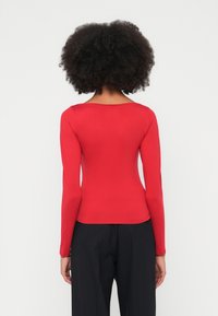 Piros hosszú ujjú, testhez simuló felső mélyen kivágott nyakkivágással, sima bordázott anyagból, magas derekú fekete nadrággal párosítva.