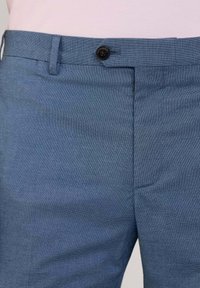 Pantaloni blu con texture e chiusura a bottone, dotati di una vita standard e vestibilità sartoriale. La foto ravvicinata mostra i dettagli del tessuto.