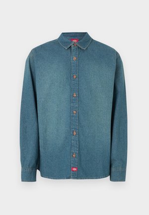 Πουκάμισο από τζιν σε μεσαίο μπλε χρώμα, με κουμπιά στο μπροστινό μέρος, μυτερό γιακά, μακριά μανίκια και καφέ κουμπιά ως διακοσμητικά στοιχεία· ετικέτα στο κάτω αριστερό μέρος.
