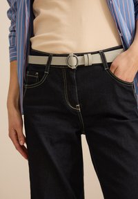 Mörkblå jeans med gul sömnad, tillsammans med ett ljust grått läderbälte med en cirkulär spänne, och en beige topp.