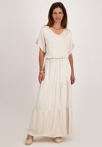Lange, crèmeskleurige maxi-jurk met korte mouwen, V-hals, gather taille en gelaagde rok. Glad materiaal en een ontspannen pasvorm.