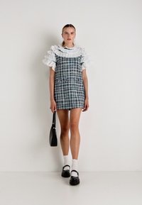 Καρό φόρεμα με λευκό ρυάκι, κοντά μανίκια και εφαρμοστή γραμμή. Φορώντας μαύρα παπούτσια και μια μικρή μαύρη τσάντα.