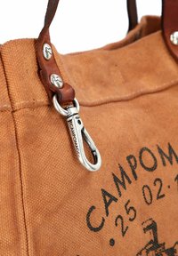 Bruine canvas tas met leren accenten, voorzien van een zilveren metalen clip, zichtbare stiksels en zwarte bedrukte tekst aan de voorkant.
