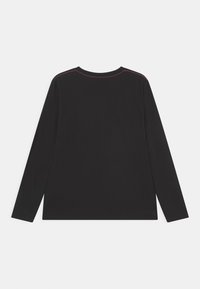 Chemise à manches longues noire en tissu doux. Elle présente un col rond et des coutures rouges contrastantes le long des coutures des épaules.