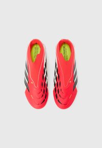 Ζευγάρι φωτεινών κόκκινων και λευκών ποδοσφαιρικών παπουτσιών με μαύρες ρίγες και υφασμένο σχέδιο, φωτογραφημένα από πάνω σε λευκό φόντο.