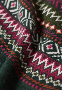 Tessuto a maglia con una base verde scuro e motivi geometrici in rosa, bianco e arancione, che incorporano zigzag e motivi floreali.