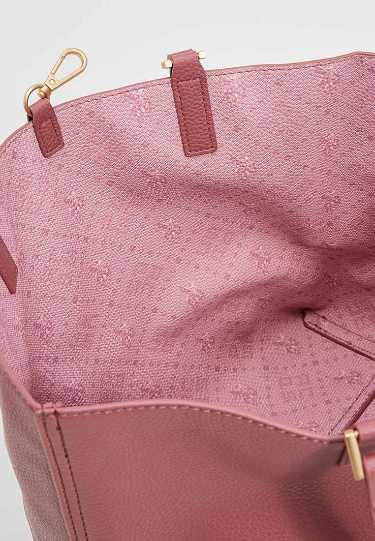 Intérieur d'un sac fourre-tout en cuir rose avec un tissu texturé affichant un motif floral subtil. Comprend des accessoires en or et des détails de sangle attachée.