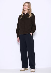 Camicia button-up in corda marrone con vestibilità rilassata e maniche lunghe, abbinata a pantaloni neri a gamba larga e sneaker beige.