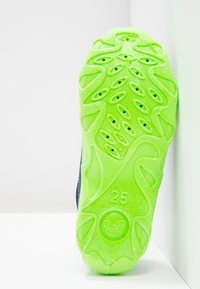 Zool van een schoen met een felgroen rubberen materiaal, een gestructureerd patroon en ventilatiegaten, met het getal "25" in reliëf.