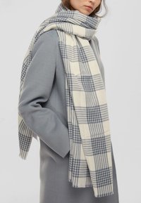 Sciarpa tessuta con un motivo a quadretti beige e navy, con bordi frangiati. Stile drappeggiato, realizzata in un materiale morbido, adatta per sovrapposizioni.