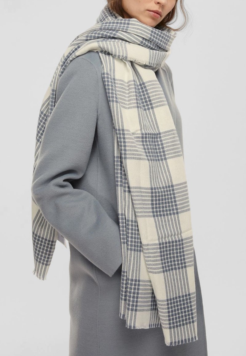 Sciarpa tessuta con un motivo a quadretti beige e navy, con bordi frangiati. Stile drappeggiato, realizzata in un materiale morbido, adatta per sovrapposizioni.