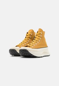 High-top sneakers made of yellow canvas with white rubber midsole and textured black outsole. Features metal eyelets and contrasting laces.