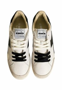 Sneakers bianchi con accenti neri, lati testurizzati e collo imbottito. Presentano lacci bianchi e neri, suole in gomma e un'etichetta con logo sulla linguetta.