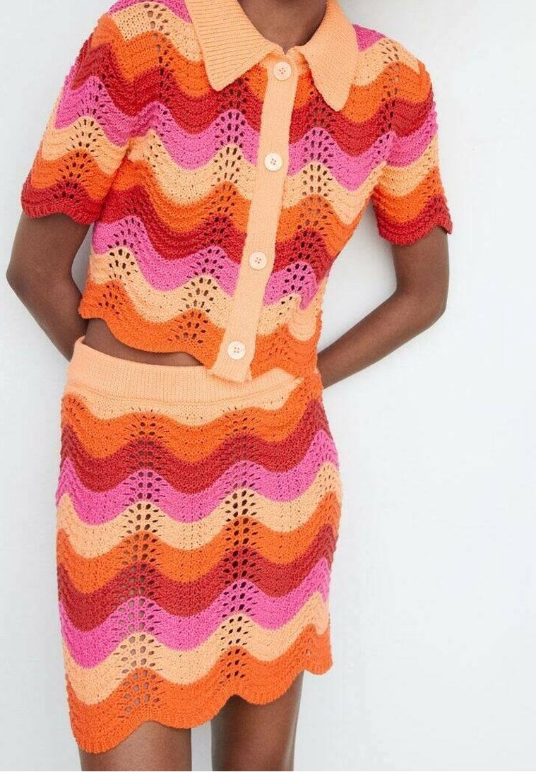 Haut en crochet à manches courtes avec boutons et jupe assortie, présentant un motif de rayures ondulées orange, rouge, rose et pêche.