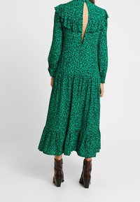Groene jurk met lange mouwen, met luipaardprint, gerimpelde schouders, open rugdetail en een rok in laagjes. Gecombineerd met bruine enkellaarzen.