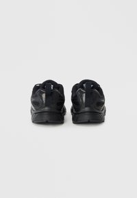 Baskets de sport noires avec un dessus en mesh, semelle en caoutchouc et col rembourré. Les caractéristiques incluent des accents texturés et une languette à l'arrière.
