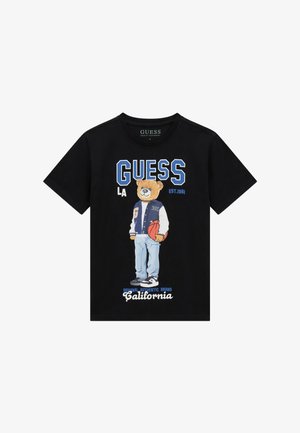 T-shirt noir avec un ours portant une veste universitaire et tenant un ballon de basket, avec les textes "GUESS LA", "Est.1981" et "California" en bleu et blanc.