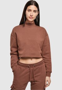 Bruin cropped sweatshirt met een hoge hals, losse pasvorm en geribbelde manchetten. Gecombineerd met bijpassende bruine joggingbroek met een elastische taille.
