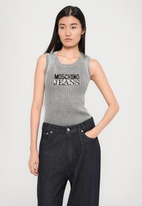 Γκρίζο ριγέ αμάνικο τοπ με "MOSCHINO JEANS" σε μαύρο χρώμα, συνδυασμένο με σκούρο τζιν παντελόνι φαρδιάς γραμμής με κουμπί και πλαϊνές τσέπες.