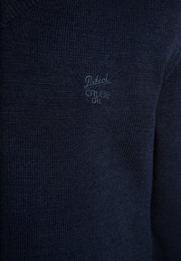 Dark blue knitted fabric with subtle embroidered text "Petrol Crude Oil" in matching thread color.