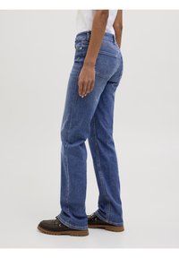 Modré denimové džíny se rovnými nohavicemi, středně vysokým pasem, pěti kapsami a viditelným šitím. Stylizováno s tmavou obuví.