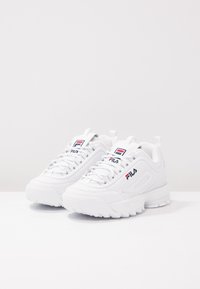 Zapatillas deportivas blancas con parte superior de cuero texturizado, lengüeta acolchada y detalle del logotipo. La suela gruesa ofrece estabilidad con un agarre pronunciado.