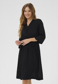 Robe noire, longueur genou, avec un décolleté en V et des manches trois-quarts. Fabriquée en tissu léger avec une taille élastique et une jupe fluide.