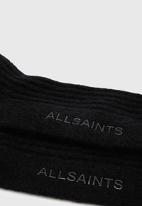Schwarze Strümpfe aus weichem Material mit geripptem Muster und geprägtem "ALLSAINTS"-Logo an der Seite.