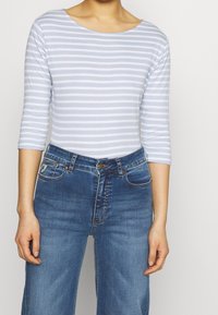 Ljust blå och vit randig långärmad topp i kombination med högmidjade mörkblå denimjeans, med fickor och en klassisk skärning.