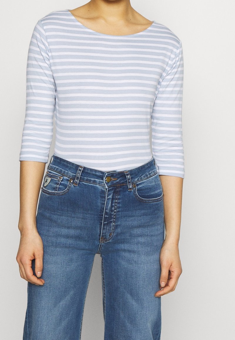 Ljust blå och vit randig långärmad topp i kombination med högmidjade mörkblå denimjeans, med fickor och en klassisk skärning.