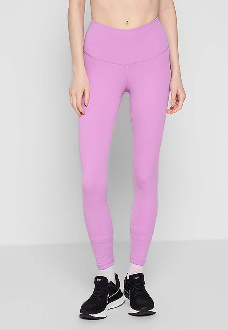 Leggings rosa a vita alta realizzati in tessuto elasticizzato, con una texture liscia e un design aderente, abbinati a scarpe da ginnastica nere.