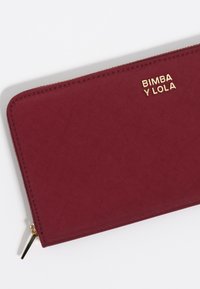 Bordowy portfel tekstylny z złotym logo "BIMBA Y LOLA", z złotym zamkiem błyskawicznym i gładkim wykończeniem.