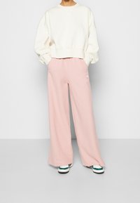 Sudadera de crema clara con hombros caídos, combinada con pantalones de chándal sueltos de un rosa pálido. Ambos presentan un sutil logotipo en blanco.