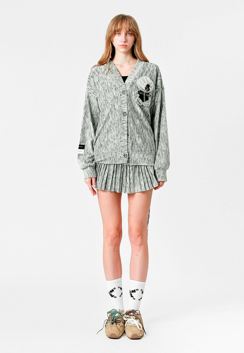 Cárdigan de punto gris con cinco botones, tejido texturizado, falda plisada y calcetines con estampado. Con detalle de flor y rayas.