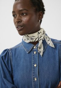 Camicia in denim con maniche a sbuffo e bottoni argento, abbinata a una sciarpa crema con fantasia annodata intorno al collo.