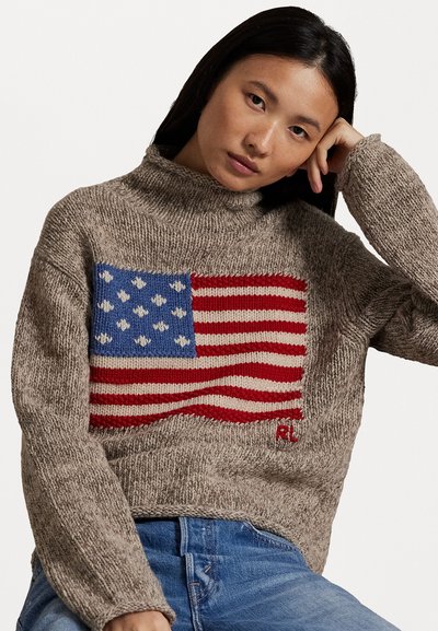Pletený sveter vo béžovej farbe s textúrovaným, nadmerným strihom. Obsahuje výrazný dizajn americkej vlajky v červenej a modrej farbe na prednej strane.