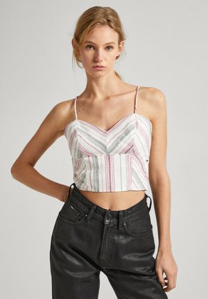 Top corto sin mangas con patrón de rayas en zigzag en rojo, negro y blanco. Cuenta con tirantes delgados ajustables y un diseño ajustado. Combinado con jeans oscuros.