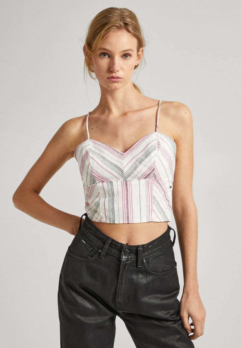 Top corto con motivo a zigzag in strisce rosse, nere e bianche. Presenta spalline sottili regolabili e un design aderente. Abbinato a jeans scuri.