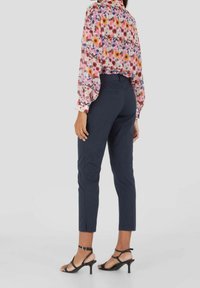 Blouse dengan pola floral dengan lengan puff panjang dalam nuansa merah muda, ungu, dan kuning, dipadukan dengan celana navy dan heels hitam bertali.