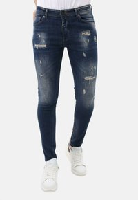 Donkerblauwe skinny jeans met verwerkte details, waaronder scheuren en vervaagde gebieden. Gecombineerd met witte veterschoenen.