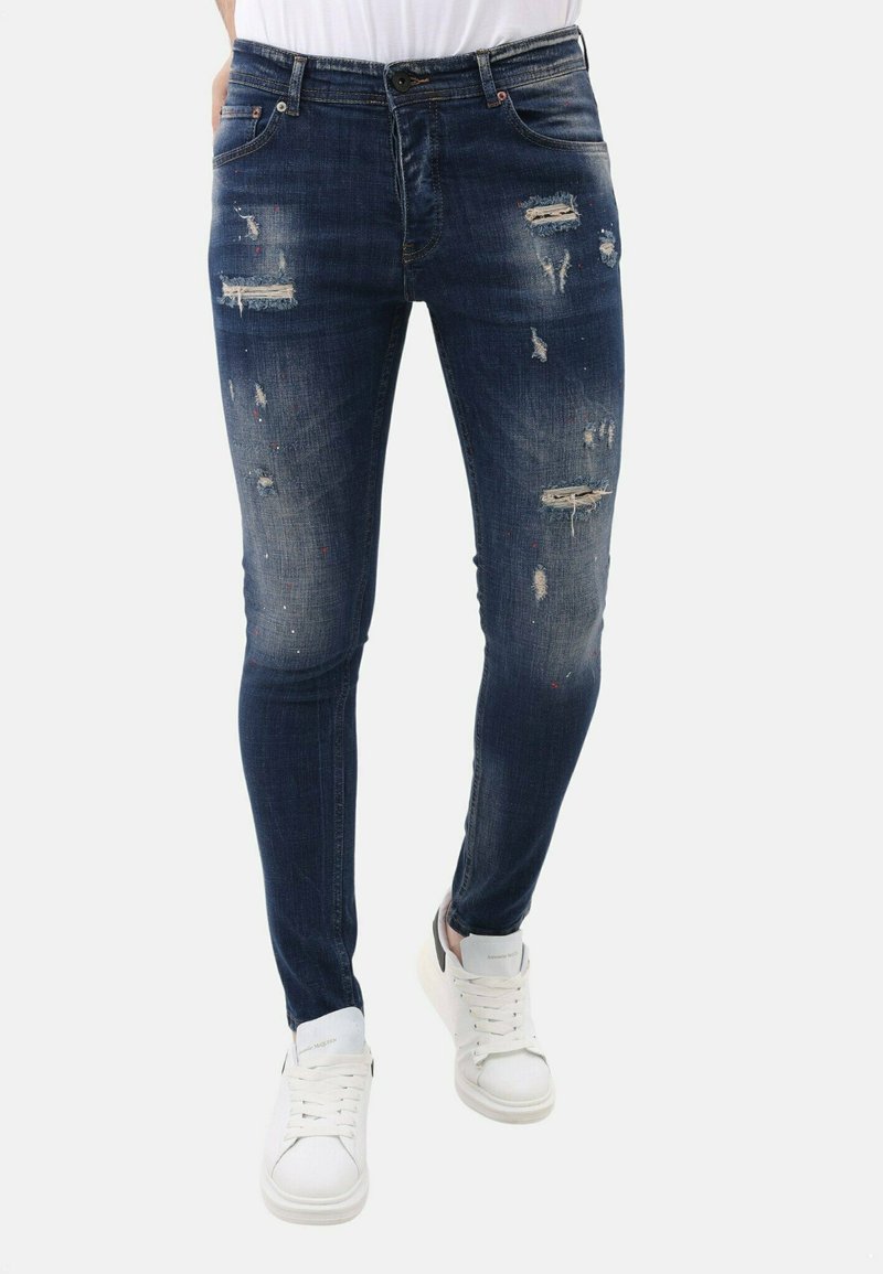 Donkerblauwe skinny jeans met verwerkte details, waaronder scheuren en vervaagde gebieden. Gecombineerd met witte veterschoenen.