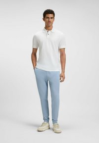 Biała koszulka polo z krótkim rękawem, jasnoniebieskie spodnie wąskie, beżowe sneakersy. Posiada klasyczny kołnierzyk z zapięciem na dwa guziki.