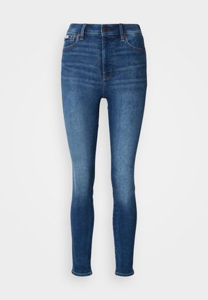 Jeans skinny blu a vita alta con bottone frontale, passanti per la cintura e dettagli scoloriti lungo le cosce e i polpacci.