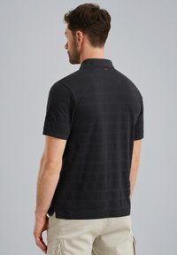Zwarte polo met korte mouwen, een gestructureerde stof met subtiele horizontale strepen en een klein logo detail op de achterkant van de kraag.