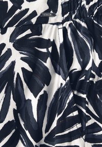 Floral patterned fabric in navy blue and white, featuring large leaf designs. Satin-like texture with a gathered waist detail. Branding visible.