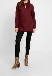 Pull col bénitier couleur marron, coupe décontractée, associé à un jean skinny noir et des bottines à imprimé serpent avec talons carrés. Texture lisse, design décontracté.