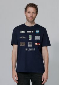 T-shirt en coton marine avec un graphisme de consoles de jeux rétro et de manettes, avec "J'AIME ÇA" imprimé en dessous en blanc.