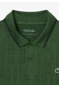 Polo verde con vestibilità slim, caratterizzato da un motivo geometrico, tessuto morbido, tre bottoni e dettagli neri a contrasto sul colletto.