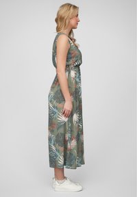 Maxi dress in green fabric featuring a floral pattern with leaves in shades of pink, white, and blue. Elastic waist and sleeveless design with sneakers.