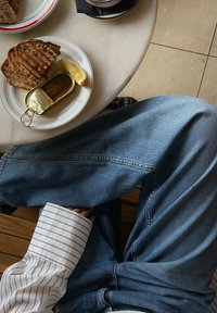 Vaaleat farkut yhdistettynä valkoiseen paitaan, jossa on sinisiä raitoja. Lautasella leipää, sitruuna ja kalapaketti marmoritasolla.